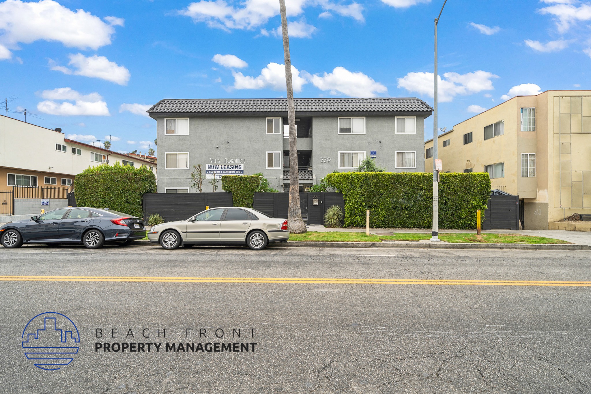 A street view with cars parked and a building with the sign "BEACH FRONT PROPERTY MANAGEMENT".